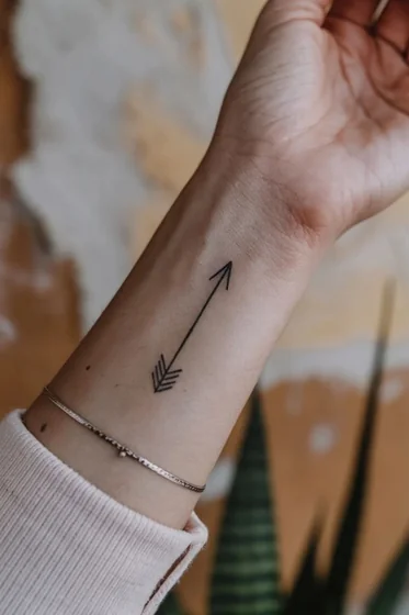 Minimalist fine line arrow tattoo design for ladies on forearm